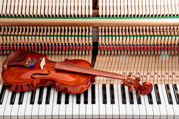 classic brown violin on the close up image of grand piano keys and interior showing strings, hammer...