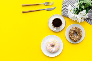 breakfast with coffee, donuts and flowers on yellow background top view mockup
