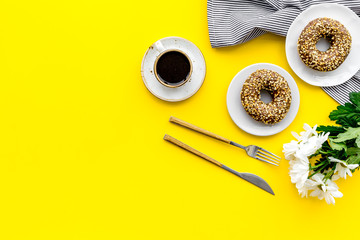 breakfast with coffee, donuts and flowers on yellow background top view mockup