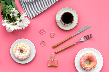 breakfast with coffee, donuts and flowers on pink background top view