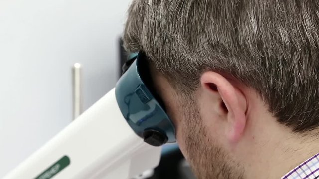 Man looks in apparatus for the treatment of spasm of accommodation, amblyopia and binocular vision disorders. Patient in ophthalmology clinic