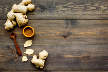 Spice and condiment. Ground ginger in small bowl near ginger root on dark wooden background top view copy space