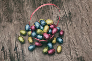 Straw basket filled with Easter chocolate eggs wrapped in colorful tinfoil on top of a wooden table