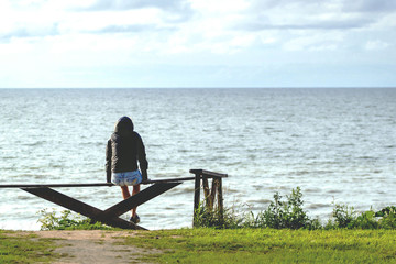 Fototapeta premium the girl sits on a bench and looks at the sea, retro toned