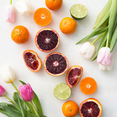 blood oranges, clementines and limes on a white background with tulips