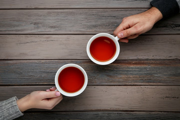 Female and male hand holding cups of tea on wooden table