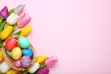 Colorful easter eggs in basket with tulips on pink background