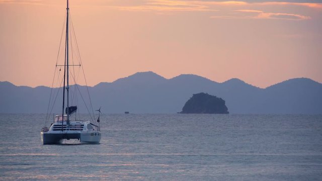 Mast yacht catamaran in the sea with islands on the background at sunset