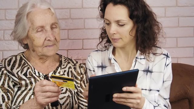 An elderly with a credit card. A young woman is teaching an old woman to use a credit card and tablet.