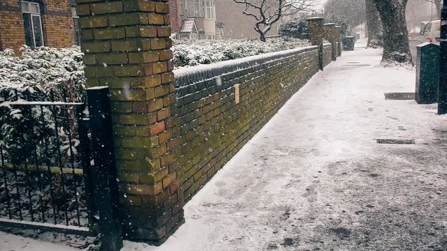 Snowfall. A brick fence along the sidewalk.