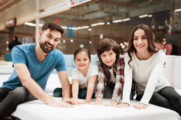 Big happy family testing orthopedic mattress in shop of furniture. Check softness of mattress.