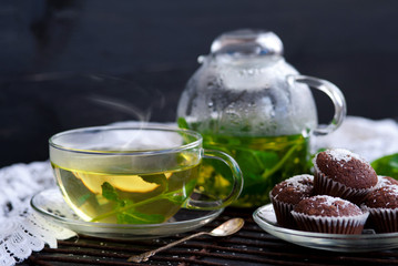 Kettle and a cup of herbal tea with mint and lemon thme, chocolate muffins with coconut