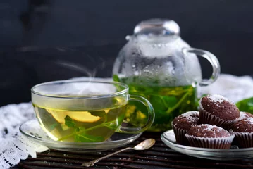 Fototapeten Kettle and a cup of herbal tea with mint and lemon thme, chocolate muffins with coconut © Inna