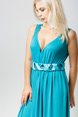 young blond girl in a beautiful cyan dress is standing in the studio