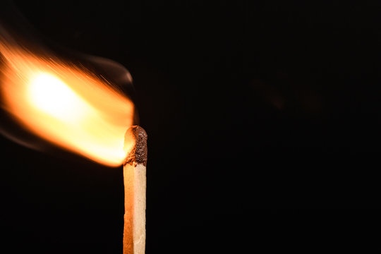 Match with strongly flaring flame beveled on its side on a black background closeup