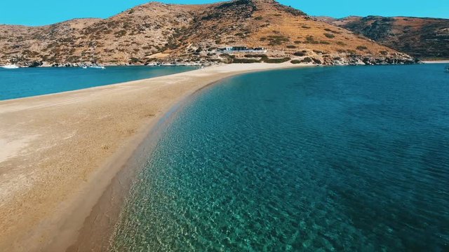 Crystal clear water of mediterranean Aegean sea and sandy coast line of Kolona beach of Kythnos island. Slow movement over surface towards the mountain with rocks and arid bushes. Kythnos, Greece