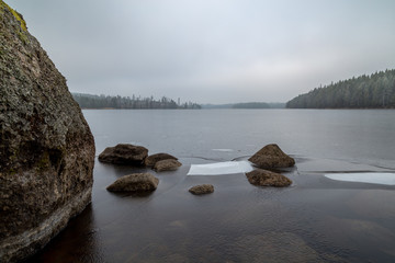 ice and stones at a small lake with forest all around
