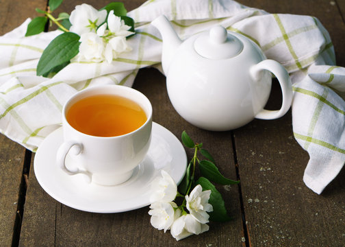 Hot green tea in a teapot and cup with a branch of jasmine flowers blossom  and white towel on rough rustic brown wooden background.  Nature healthy slow life concept.