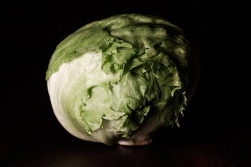raw green iceberg lettuce on dark brown wooden desk in spotlight - close up