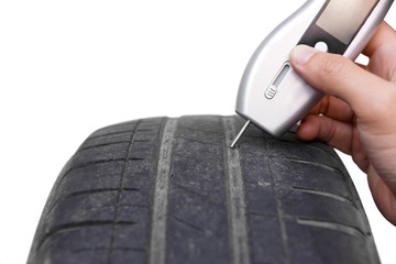 Using a digital tire tread depth measuring tool with old tire isolated on white / Road safety and...