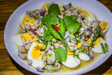Egg Yum on a plate on old wooden background.Close up salted eggs with spicy and sour salad in Thai style cuisine that called Yum Kai