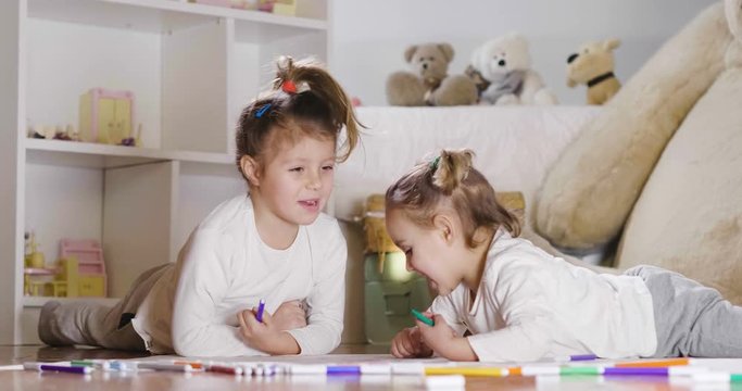 Portrait of two little girl lying on the floor in their bedroom that color with felt-tip pens and make artistic drawings. Concept of: family, color, creativity, art, happiness and educational.