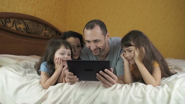 Happy family with a gadget. Family on the Internet. The parents with the children lie on the bed with the tablet.