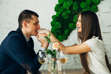 Cheerful young man and woman are dating in restaurant. They are sitting at the table and looking at each other with love.