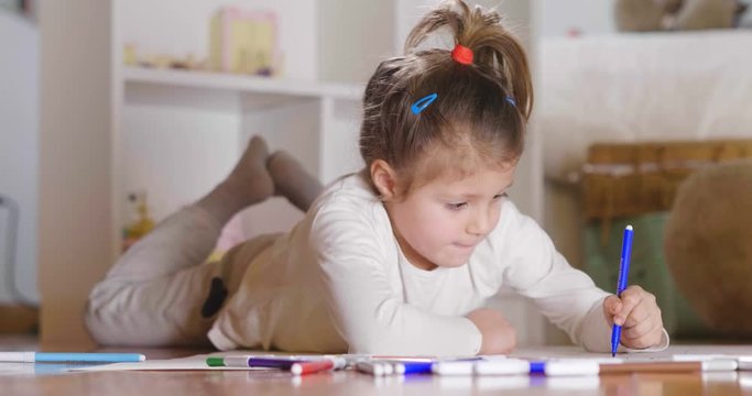 Portrait of two little girl lying on the floor in their bedroom that color with felt-tip pens and make artistic drawings. Concept of: family, color, creativity, art, happiness and educational.