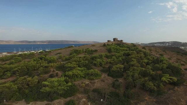 Flight over hill with green bushes, trees and ruins of a historic fortress on top near the town of Lavrio and Aegean sea coast line. Attica, Greece. Aerial footage.