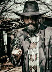 Fototapeta premium Cowboy holding up a gun, standing outside in an old west, western scene.