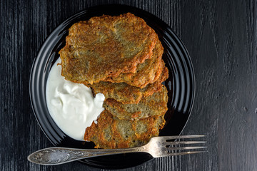 potato pancakes with sour cream, on a black plate on a wooden background. Home kitchen.