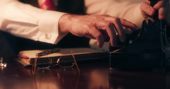 Reading glasses are placed on a desk by their owner who proceeds to make a business call on his rotary style vintage desktop telephone.