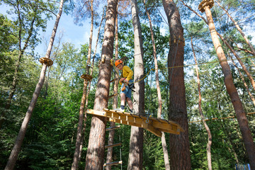 Fototapeta premium adventure climbing high wire park - boy on course in mountain helmet and safety equipment