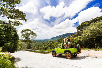 two girls best friends travel on a tropical island in a car with an open top are having fun having a smile. enjoyment travel, excursion summer dressed shorts T-shirts sunglasses, blue sky
