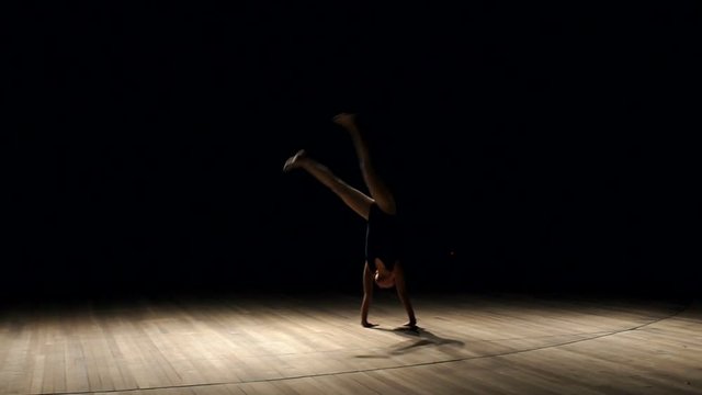 Little girl gymnast doing a somersault in the studio on a black background, slow motion.