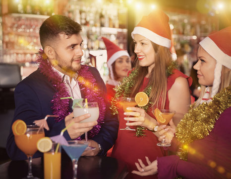 Man and two women with cocktails in Santa hats celebrating at ni