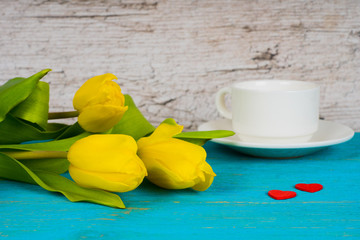 yellow tulips with coffee cup and two red hearts on turquoise wooden table