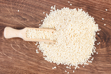Heap of sesame seeds with wooden scoop on board