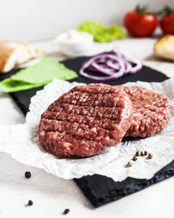 Ingredients for making hamburger. Raw burger beef cutlet, two buns, fried onion, fresh spinach and ketchup sauce on dark chopping board over old wooden background. Space for text.