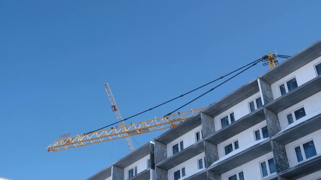 Construction of a multi-storey building. Cranes turns to the side over the roof in sky background.