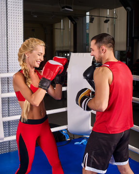 Boxing workout woman in fitness class ring. Man trainer holding sport mitts in gym. Sport female box gloves are red backview. Love couple trains together.