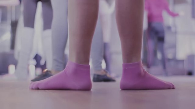 Warm up before dancing. Legs in pink socks in a dance position. A group of people in the dance hall
