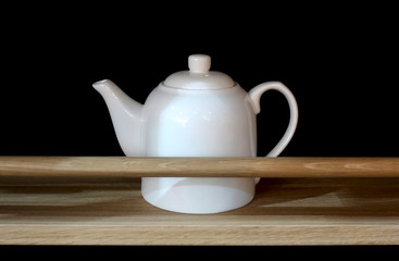 White ceramic teapot on a wooden shelf on a black background