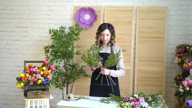 Florist at work: pretty young blond woman holds fashion modern bouquet of different flowers with peone and roses in craft paper