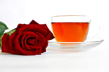 hot black tea in transparent glass cup on saucer with red rose on white background