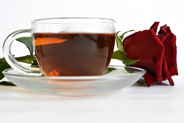 hot black tea in transparent glass cup on dish and red rose on white background