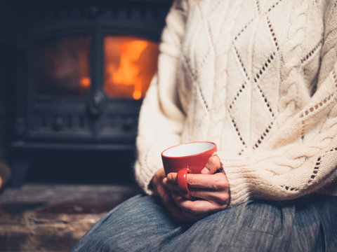 Woman in white jumper by fireplace with mug