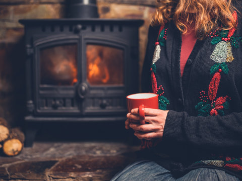 Woman in christmas jumper with mug by fire