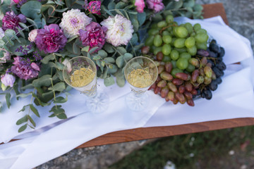 Romantic dinner outdoors. Glasses with champagne, grapes and a lot of flowers on wooden board.